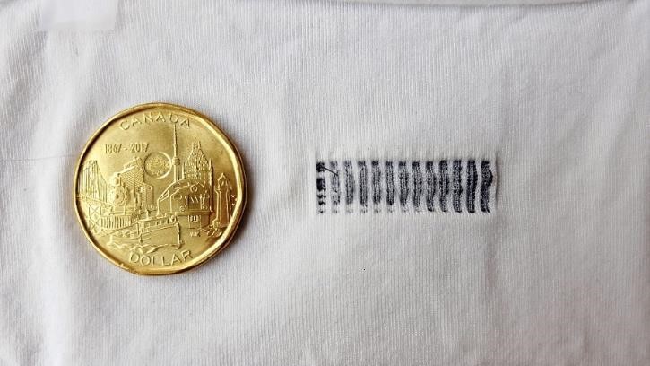 Canadian one-dollar coin and thirteen strain sensors that can be woven into fabric, to illustrate how small the sensors are